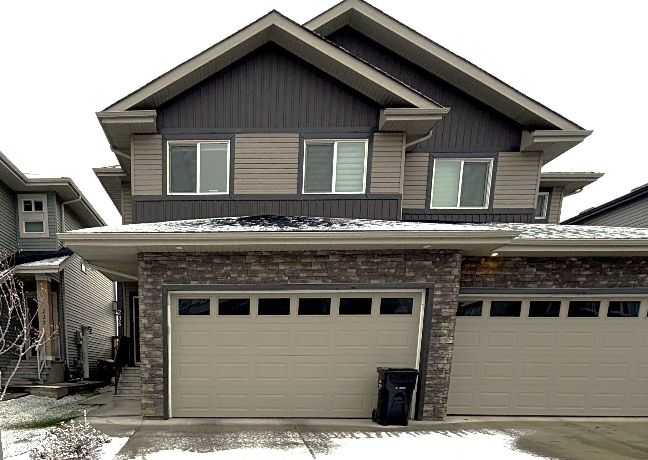 A house with a grey garage door and a brick pillar.